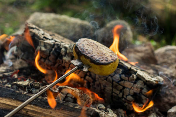 Teleskopisk grillpinne med potatis över lägerelden.