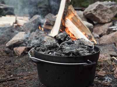 Dutch oven med kol på locket framför lägerelden.