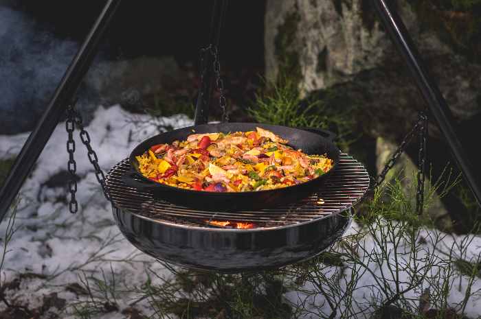 Paella tillagad i gjutjärnspanna över en Braspanna.