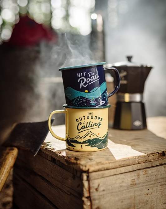 Emaljmugg retro med tryck The outdoor is calling - här tillsammans med en annan mugg på en trälåda.
